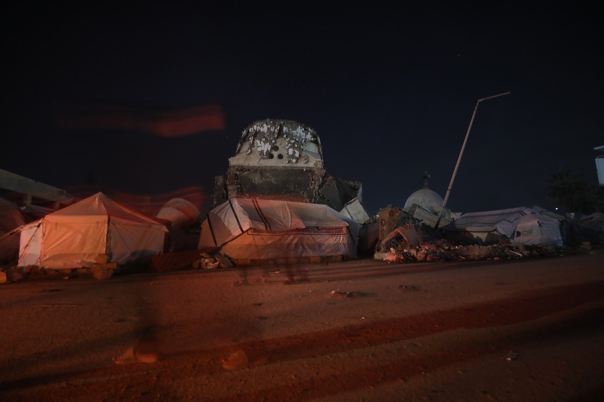 يسير فلسطينيون في أحد شوارع مدينة غزة، بينما يكافح النازحون في خيامهم لمواجهة الظلام، يتدفؤون ويطهون طعامهم بالحطب، محرومين حتى من أبسط مقومات الحياة، 23 يناير/كانون الثاني 2020. صورة: عمر أشتوي