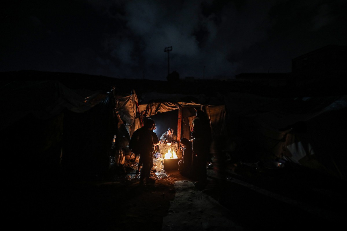 يسير فلسطينيون في أحد شوارع مدينة غزة، بينما يكافح النازحون في خيامهم لمواجهة الظلام، يتدفؤون ويطهون طعامهم بالحطب، محرومين حتى من أبسط مقومات الحياة، 19 يناير/كانون الثاني 2026. صورة: عمر أشتوي