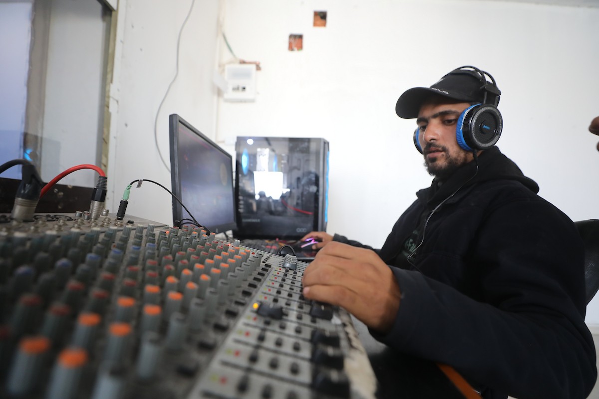 مذيع راديو فلسطيني يبث عبر الإنترنت من استوديوهات إذاعة صوت القدس في غزة، 24 يناير/كانون الثاني 2026. عادت الإذاعة إلى البث بعد توقف دام عامين بسبب الحرب، معتمدةً على معدات بسيطة للتواصل مع الجمهور المحلي ونقل الأخبار عن الأوضاع الإنسانية في القطاع. صورة: عمر أشتوي