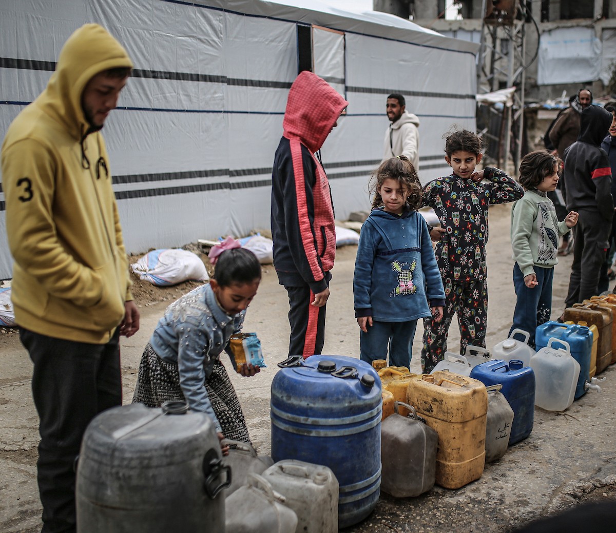يملأ الفلسطينيون جالوناتهم بالمياه التي توزعها صهاريج المياه، وينقلونها إلى خيامهم في مخيم النصيرات، حيث تفاقمت أزمة المياه نتيجة الأضرار الجسيمة التي لحقت بالبنية التحتية جراء الهجمات الإسرائيلية. النصيرات، وسط قطاع غزة، 29 يناير/كانون الثاني 2026. صورة: رمزي أبو عامر