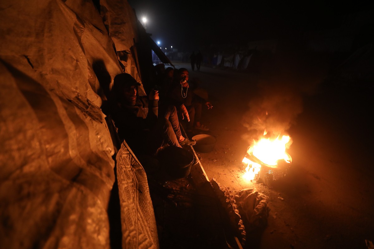 يسير فلسطينيون في أحد شوارع مدينة غزة، بينما يكافح النازحون في خيامهم لمواجهة الظلام، يتدفؤون ويطهون طعامهم بالحطب، محرومين حتى من أبسط مقومات الحياة، 23 يناير/كانون الثاني 2020. صورة: عمر أشتوي