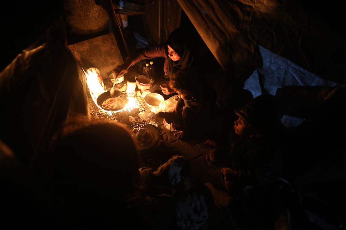 يسير فلسطينيون في أحد شوارع مدينة غزة، بينما يكافح النازحون في خيامهم لمواجهة الظلام، يتدفؤون ويطهون طعامهم بالحطب، محرومين حتى من أبسط مقومات الحياة، 23 يناير/كانون الثاني 2020. صورة: عمر أشتوي