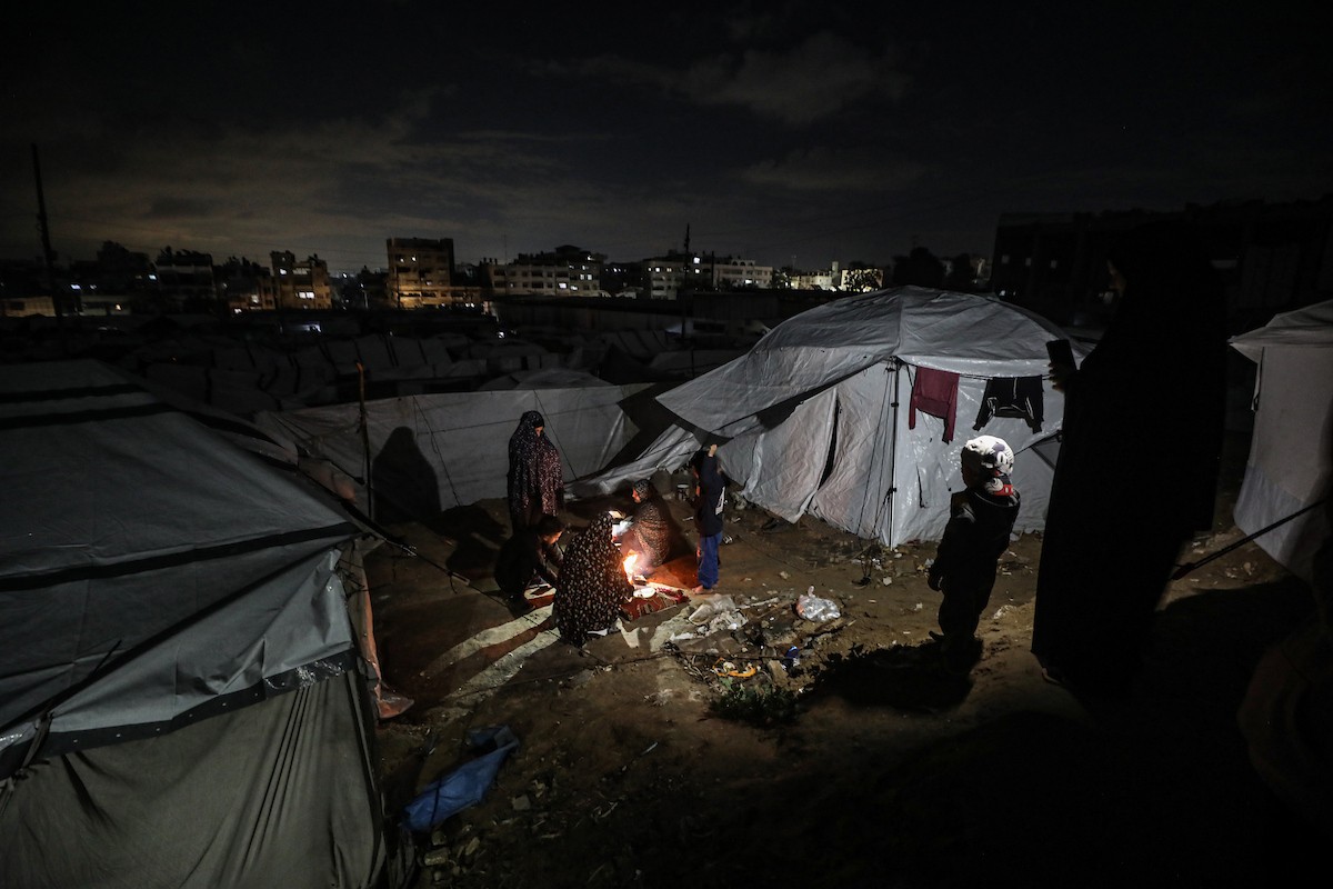 يسير فلسطينيون في أحد شوارع مدينة غزة، بينما يكافح النازحون في خيامهم لمواجهة الظلام، يتدفؤون ويطهون طعامهم بالحطب، محرومين حتى من أبسط مقومات الحياة، 19 يناير/كانون الثاني 2026. صورة: عمر أشتوي