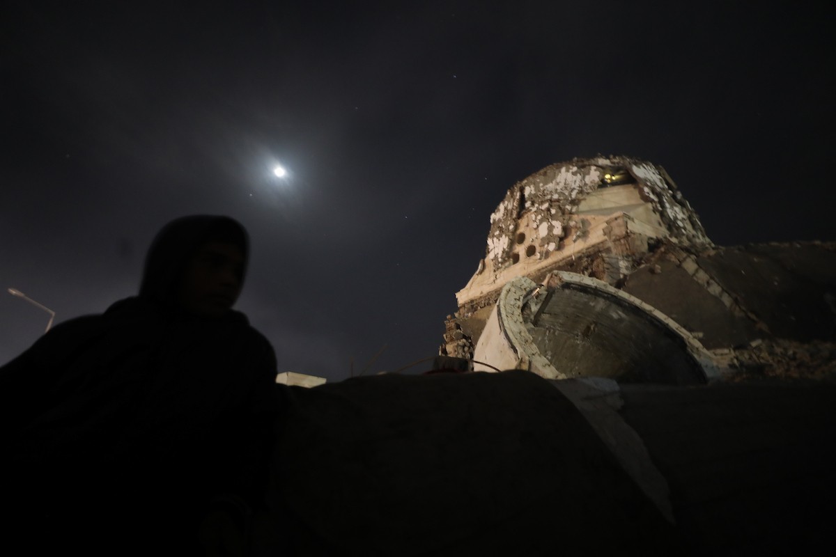 يسير فلسطينيون في أحد شوارع مدينة غزة، بينما يكافح النازحون في خيامهم لمواجهة الظلام، يتدفؤون ويطهون طعامهم بالحطب، محرومين حتى من أبسط مقومات الحياة، 23 يناير/كانون الثاني 2020. صورة: عمر أشتوي