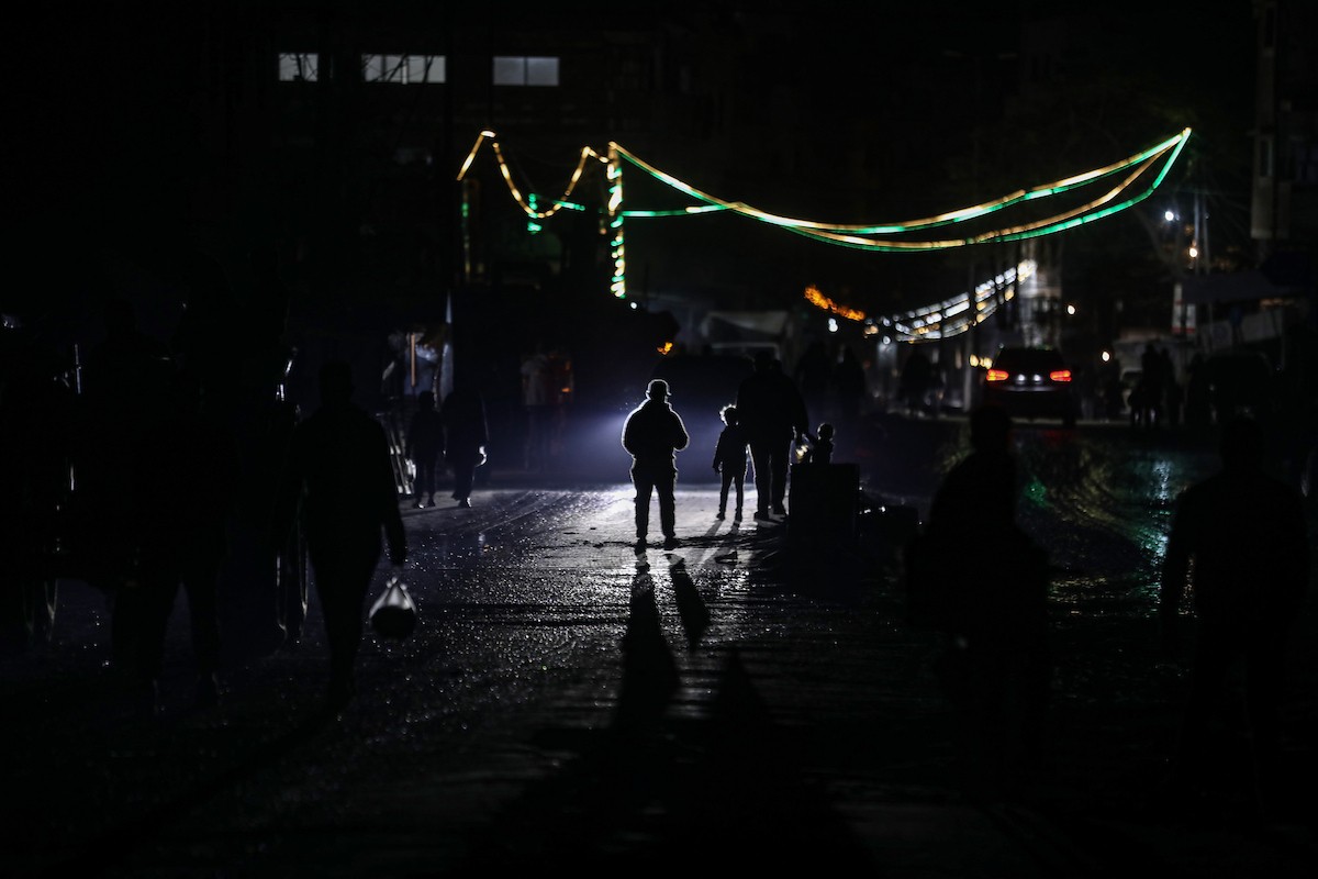يسير فلسطينيون في أحد شوارع مدينة غزة، بينما يكافح النازحون في خيامهم لمواجهة الظلام، يتدفؤون ويطهون طعامهم بالحطب، محرومين حتى من أبسط مقومات الحياة، 19 يناير/كانون الثاني 2026. صورة: عمر أشتوي