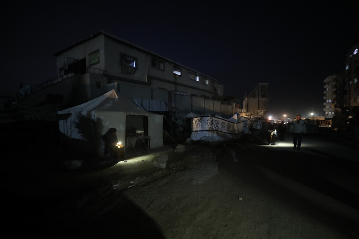 يسير فلسطينيون في أحد شوارع مدينة غزة، بينما يكافح النازحون في خيامهم لمواجهة الظلام، يتدفؤون ويطهون طعامهم بالحطب، محرومين حتى من أبسط مقومات الحياة، 23 يناير/كانون الثاني 2020. صورة: عمر أشتوي