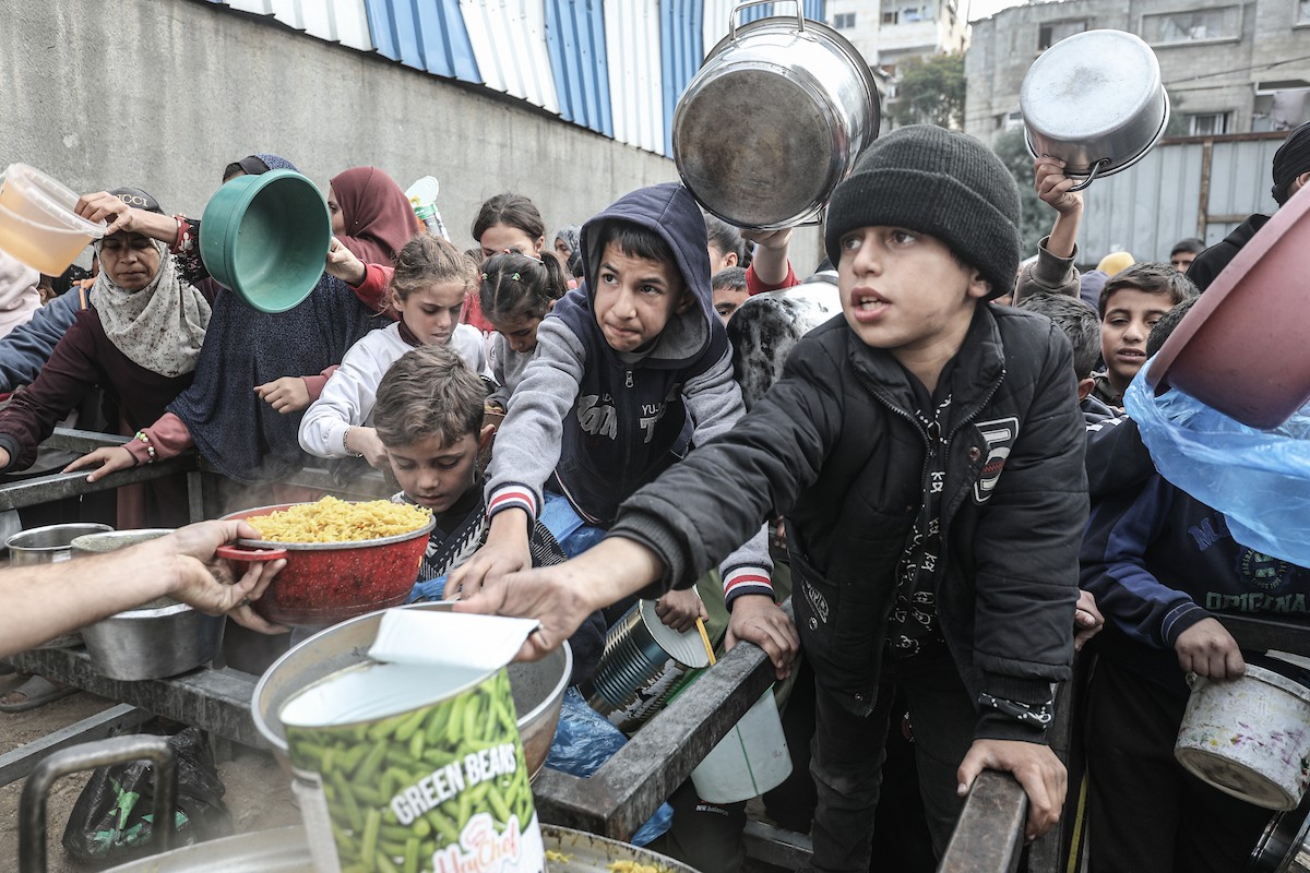 أطفال فلسطينيون ينتظرون وجبة ساخنة، توزعها إحدى المنظمات الخيرية، في ظل استمرار أزمة الغذاء بسبب محدودية المساعدات الإنسانية في مخيم النصيرات للاجئين وسط قطاع غزة، في 10 يناير/كانون الثاني 2026. صورة: معز صالحي