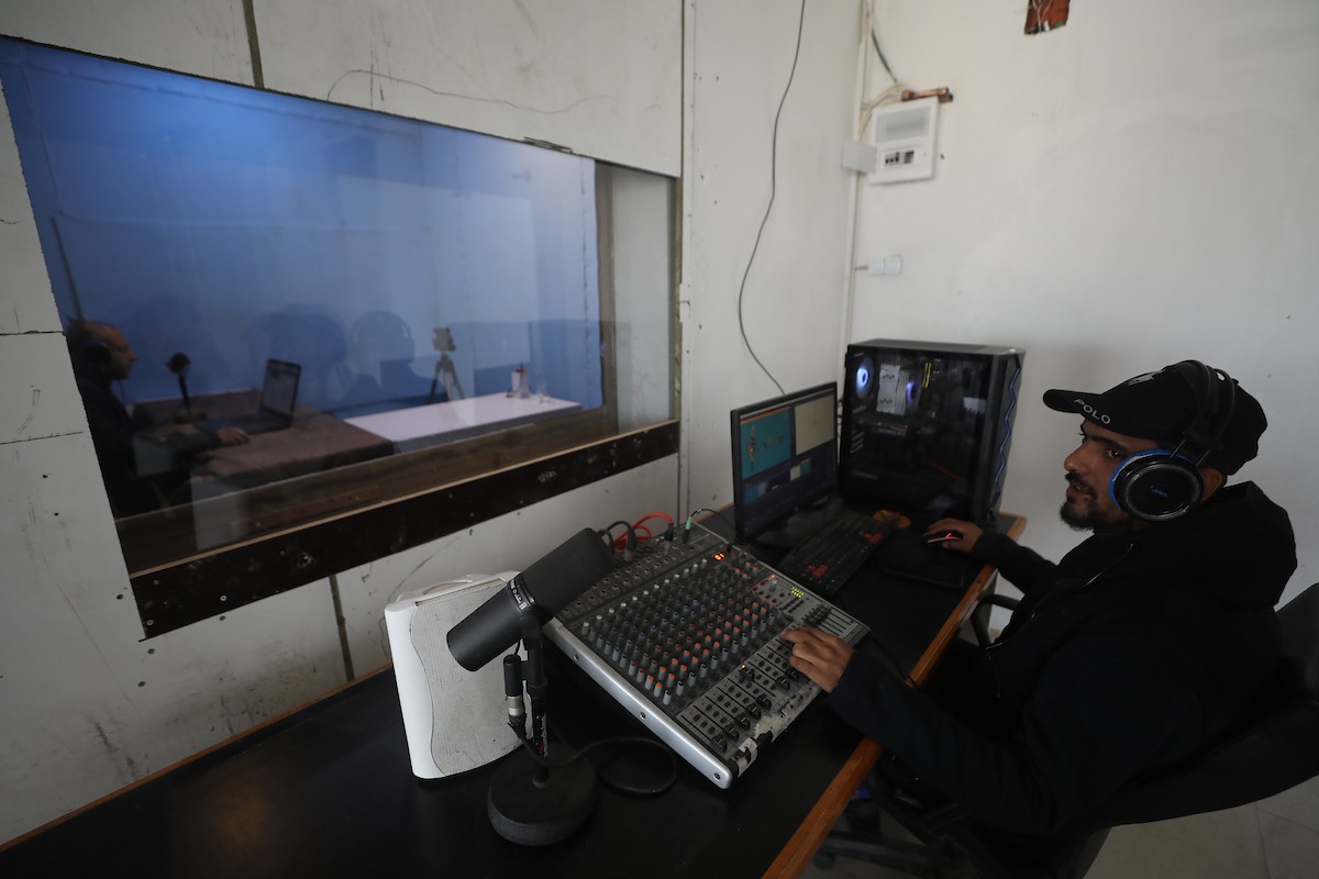 مذيع راديو فلسطيني يبث عبر الإنترنت من استوديوهات إذاعة صوت القدس في غزة، 24 يناير/كانون الثاني 2026. عادت الإذاعة إلى البث بعد توقف دام عامين بسبب الحرب، معتمدةً على معدات بسيطة للتواصل مع الجمهور المحلي ونقل الأخبار عن الأوضاع الإنسانية في القطاع. صورة: عمر أشتوي