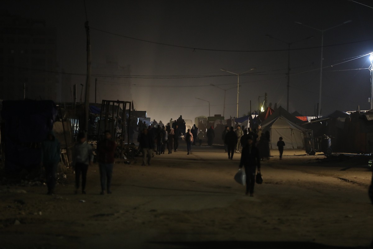 يسير فلسطينيون في أحد شوارع مدينة غزة، بينما يكافح النازحون في خيامهم لمواجهة الظلام، يتدفؤون ويطهون طعامهم بالحطب، محرومين حتى من أبسط مقومات الحياة، 23 يناير/كانون الثاني 2020. صورة: عمر أشتوي