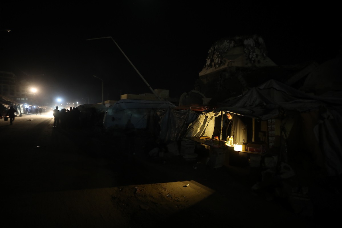 يسير فلسطينيون في أحد شوارع مدينة غزة، بينما يكافح النازحون في خيامهم لمواجهة الظلام، يتدفؤون ويطهون طعامهم بالحطب، محرومين حتى من أبسط مقومات الحياة، 23 يناير/كانون الثاني 2020. صورة: عمر أشتوي