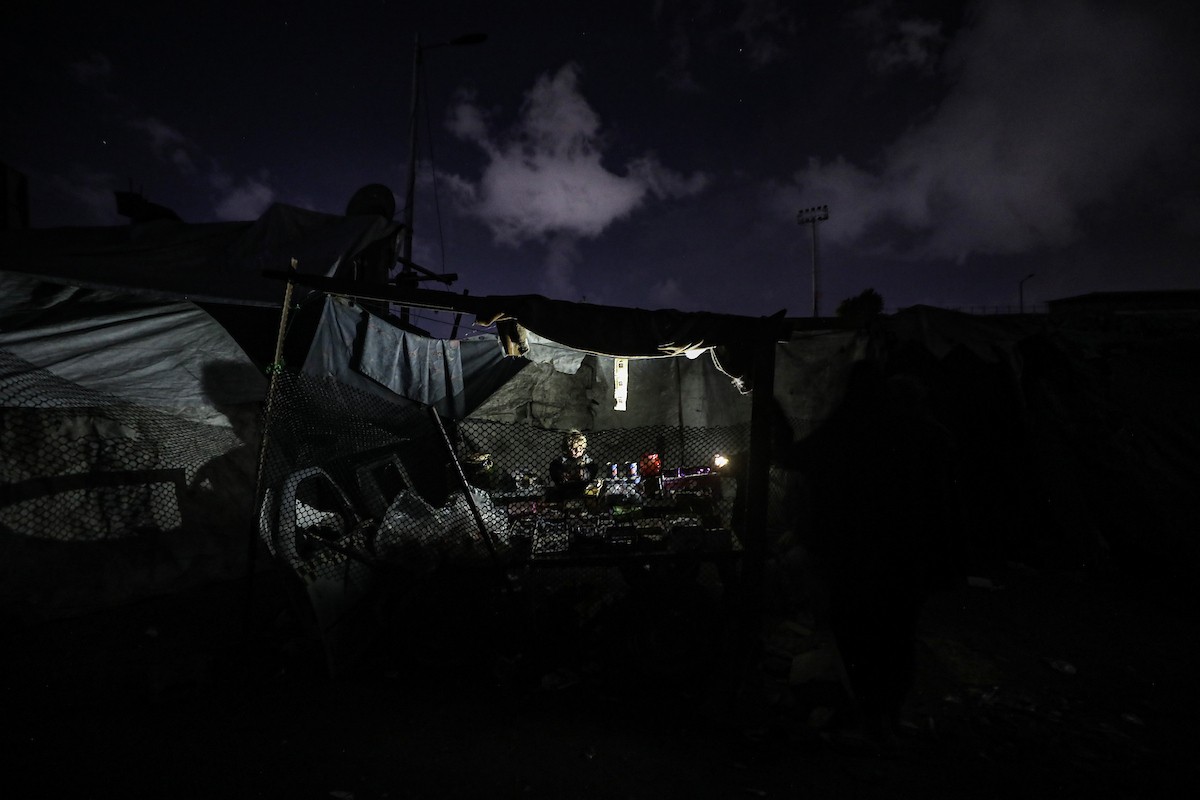 يسير فلسطينيون في أحد شوارع مدينة غزة، بينما يكافح النازحون في خيامهم لمواجهة الظلام، يتدفؤون ويطهون طعامهم بالحطب، محرومين حتى من أبسط مقومات الحياة، 19 يناير/كانون الثاني 2026. صورة: عمر أشتوي