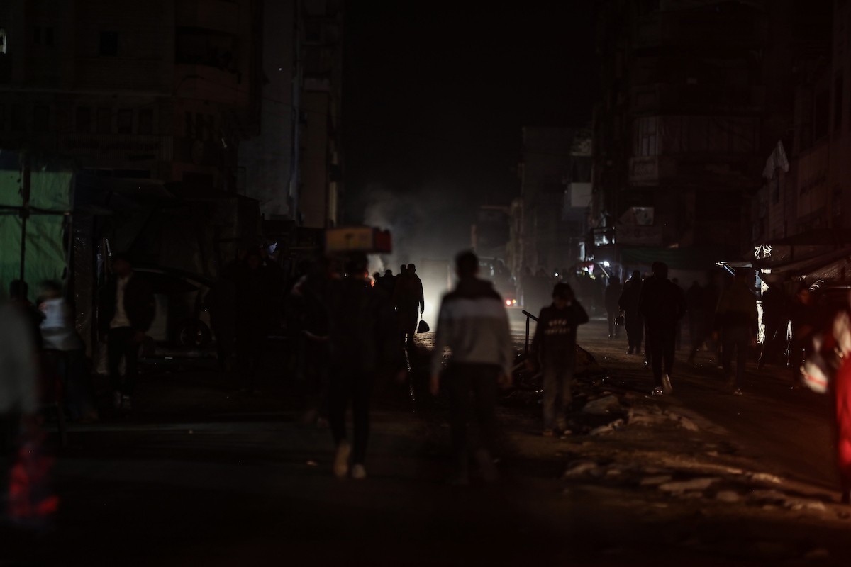 يسير فلسطينيون في أحد شوارع مدينة غزة، بينما يكافح النازحون في خيامهم لمواجهة الظلام، يتدفؤون ويطهون طعامهم بالحطب، محرومين حتى من أبسط مقومات الحياة، 19 يناير/كانون الثاني 2026. صورة: عمر أشتوي