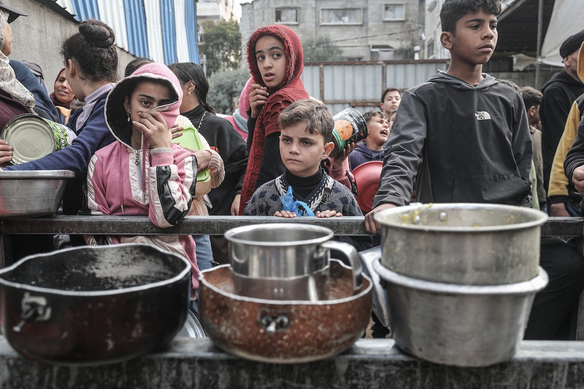 أطفال فلسطينيون ينتظرون وجبة ساخنة، توزعها إحدى المنظمات الخيرية، في ظل استمرار أزمة الغذاء بسبب محدودية المساعدات الإنسانية في مخيم النصيرات للاجئين وسط قطاع غزة، في 10 يناير/كانون الثاني 2026. صورة: معز صالحي
