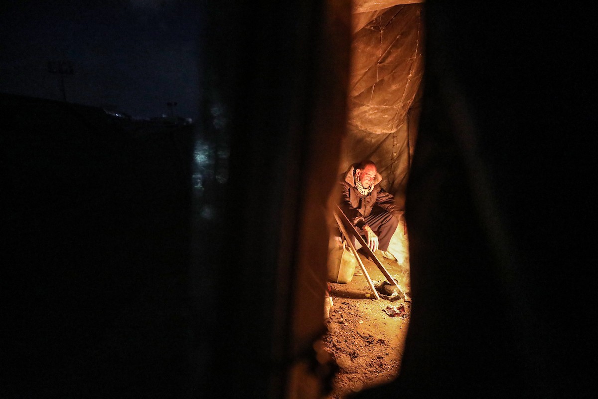 يسير فلسطينيون في أحد شوارع مدينة غزة، بينما يكافح النازحون في خيامهم لمواجهة الظلام، يتدفؤون ويطهون طعامهم بالحطب، محرومين حتى من أبسط مقومات الحياة، 19 يناير/كانون الثاني 2026. صورة: عمر أشتوي