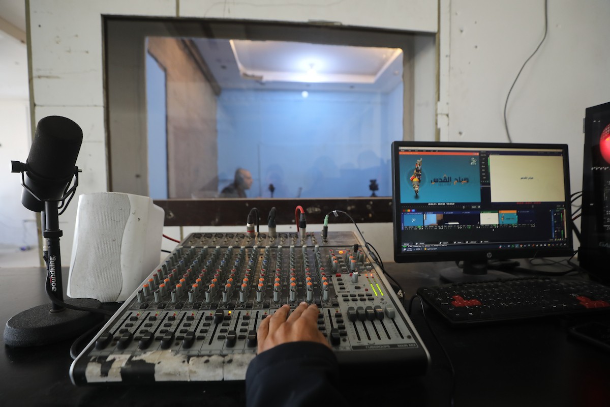 مذيع راديو فلسطيني يبث عبر الإنترنت من استوديوهات إذاعة صوت القدس في غزة، 24 يناير/كانون الثاني 2026. عادت الإذاعة إلى البث بعد توقف دام عامين بسبب الحرب، معتمدةً على معدات بسيطة للتواصل مع الجمهور المحلي ونقل الأخبار عن الأوضاع الإنسانية في القطاع. صورة: عمر أشتوي