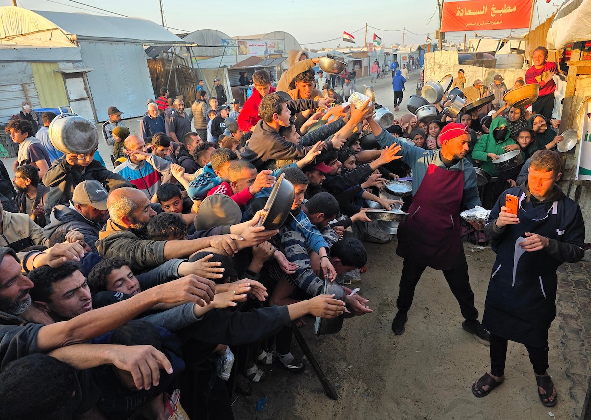 فلسطينيون نازحون يكافحون للحصول على طعام مُتبرع به للإفطار، وجبة كسر الصيام، في اليوم الرابع من شهر رمضان المبارك في مطبخ مجتمعي في خان يونس، قطاع غزة، 21 فبراير/شباط 2026. تصوير: طارق محمد/(APA Images)