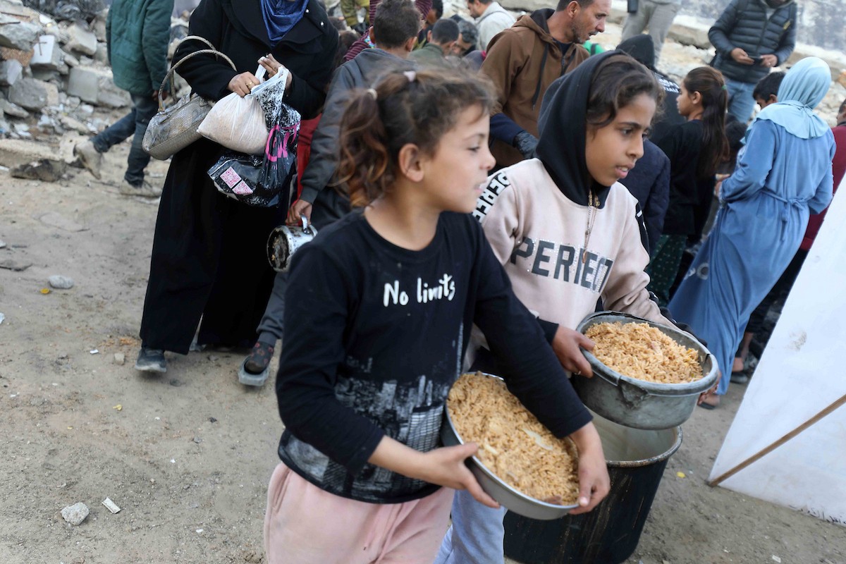 تجمع فلسطينيون نازحون، بينهم أطفال ونساء، حاملين أوعية طعام لتلقي وجبات ساخنة وزعتها جمعيات خيرية قبل الإفطار في مدينة غزة في 27 فبراير/شباط 2026.صورة: عمر أشتوي