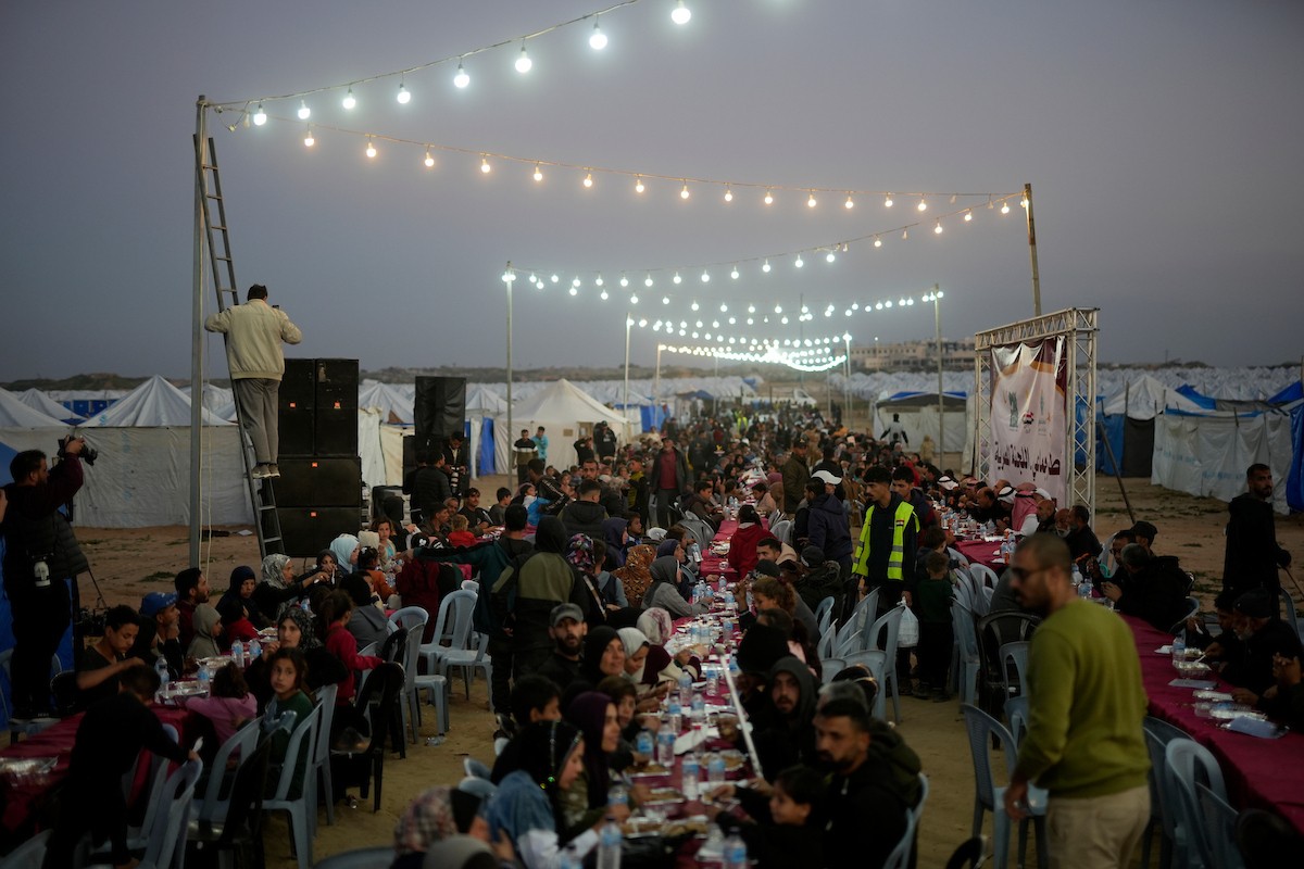 يتجمع فلسطينيون نازحون لتناول وجبة الإفطار، وهي وجبة كسر الصيام، خلال شهر رمضان المبارك في مخيم خيام يؤويهم، بحي الزهراء وسط قطاع غزة، يوم السبت 21 فبراير/شباط 2026. تصوير: عمر أشتوي