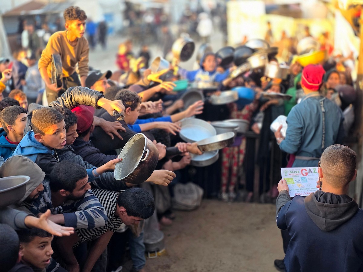 فلسطينيون نازحون يكافحون للحصول على طعام مُتبرع به للإفطار، وجبة كسر الصيام، في اليوم الرابع من شهر رمضان المبارك في مطبخ مجتمعي في خان يونس، قطاع غزة، 21 فبراير/شباط 2026. تصوير: طارق محمد/(APA Images)