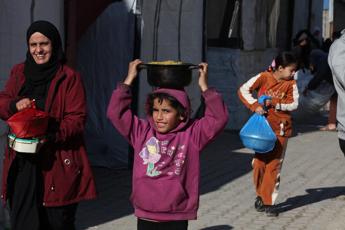 يتجمع فلسطينيون لتناول وجبة ساخنة وزعتها إحدى الجمعيات الخيرية، وسط أزمة غذائية مستمرة بسبب محدودية المساعدات الإنسانية خلال شهر رمضان في مخيم النصيرات للاجئين وسط قطاع غزة. ٢٣ فبرايرشباط ٢٠٢٦. تصوير معز صالحي
