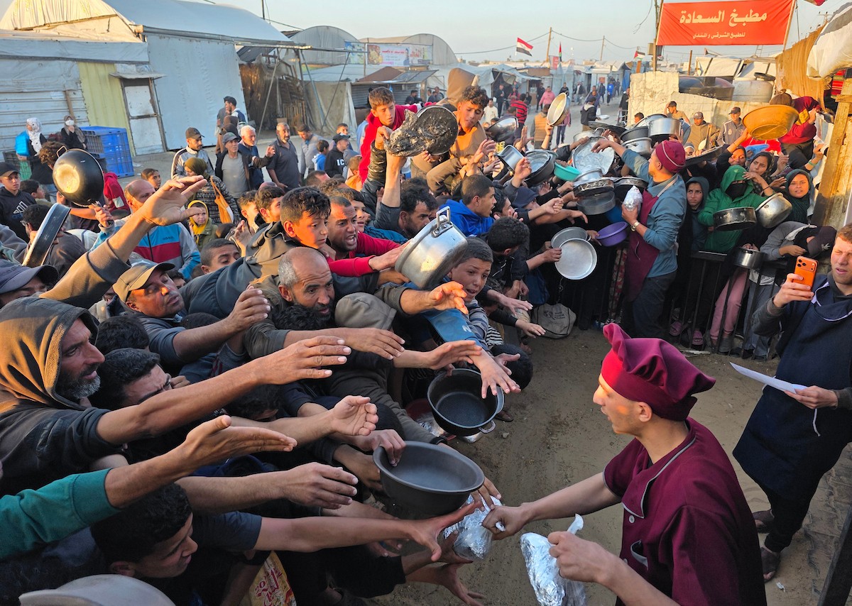 فلسطينيون نازحون يكافحون للحصول على طعام مُتبرع به للإفطار، وجبة كسر الصيام، في اليوم الرابع من شهر رمضان المبارك في مطبخ مجتمعي في خان يونس، قطاع غزة، 21 فبراير/شباط 2026. تصوير: طارق محمد/(APA Images)