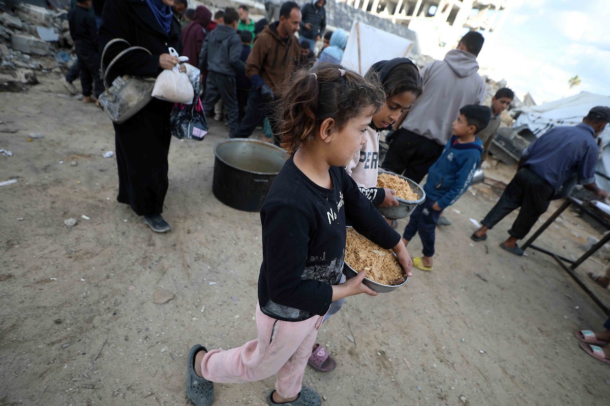 تجمع فلسطينيون نازحون، بينهم أطفال ونساء، حاملين أوعية طعام لتلقي وجبات ساخنة وزعتها جمعيات خيرية قبل الإفطار في مدينة غزة في 27 فبراير/شباط 2026.صورة: عمر أشتوي