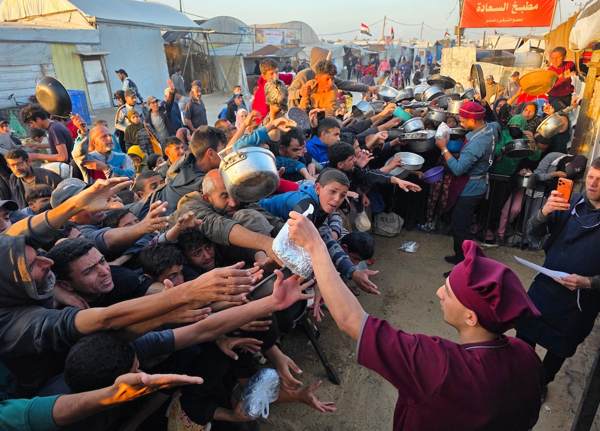 فلسطينيون نازحون يكافحون للحصول على طعام مُتبرع به للإفطار، وجبة كسر الصيام، في اليوم الرابع من شهر رمضان المبارك في مطبخ مجتمعي في خان يونس، قطاع غزة، 21 فبراير/شباط 2026. تصوير: طارق محمد/(APA Images)