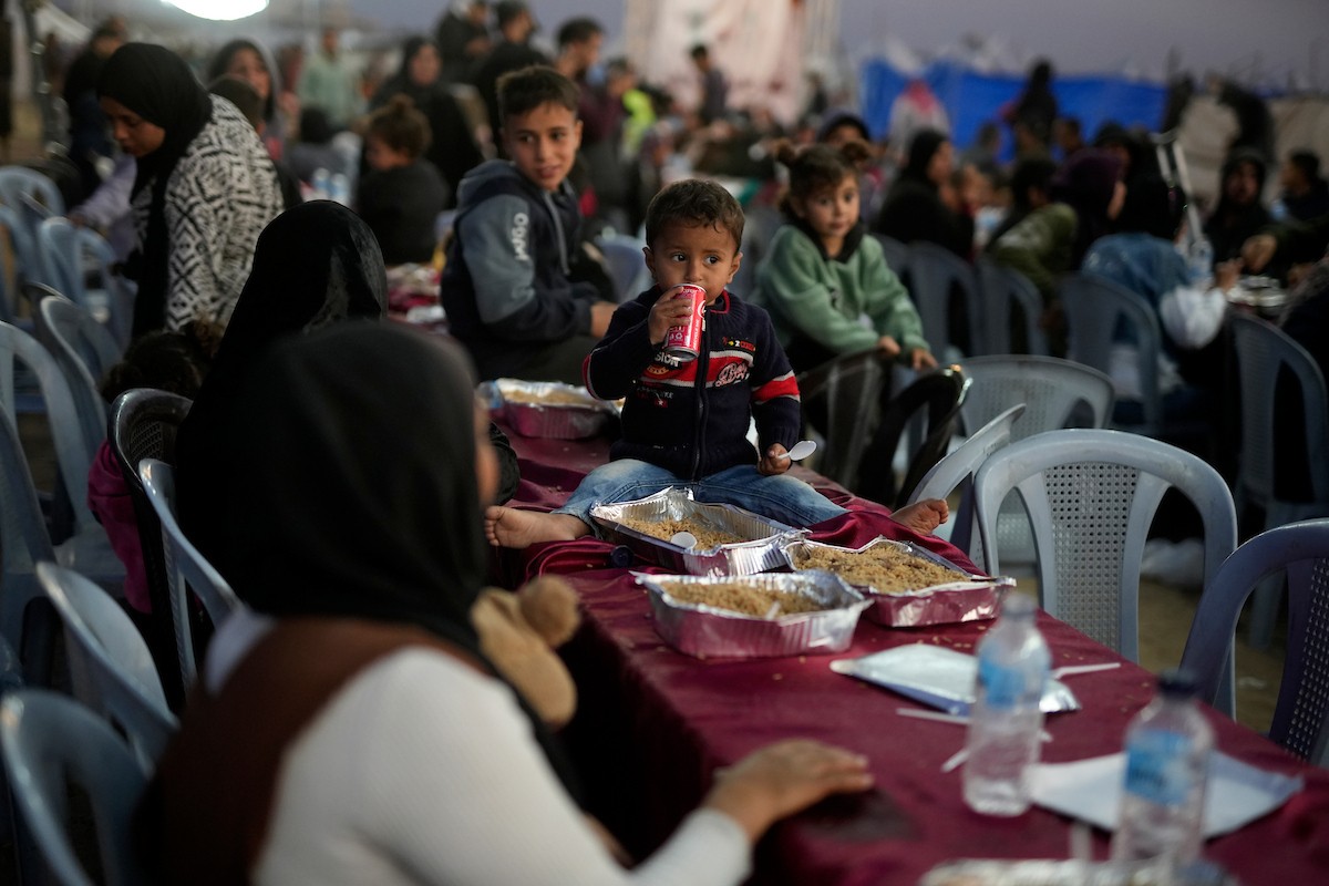 يتجمع فلسطينيون نازحون لتناول وجبة الإفطار، وهي وجبة كسر الصيام، خلال شهر رمضان المبارك في مخيم خيام يؤويهم، بحي الزهراء وسط قطاع غزة، يوم السبت 21 فبراير/شباط 2026. تصوير: عمر أشتوي