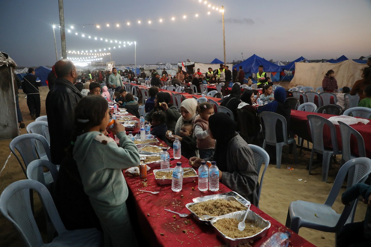 يتجمع فلسطينيون نازحون لتناول وجبة الإفطار، وهي وجبة كسر الصيام، خلال شهر رمضان المبارك في مخيم خيام يؤويهم، بحي الزهراء وسط قطاع غزة، يوم السبت 21 فبراير/شباط 2026. تصوير: عمر أشتوي