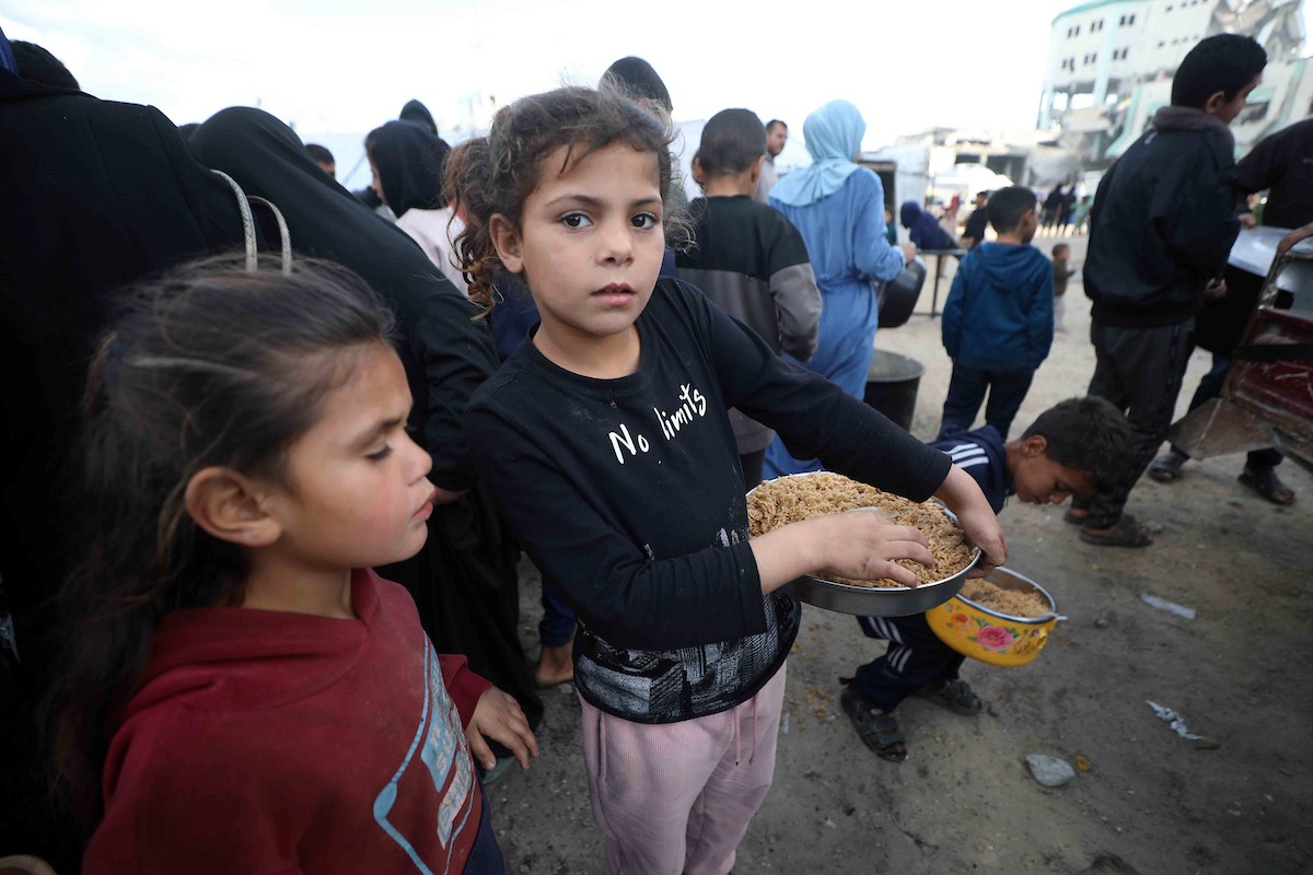 تجمع فلسطينيون نازحون، بينهم أطفال ونساء، حاملين أوعية طعام لتلقي وجبات ساخنة وزعتها جمعيات خيرية قبل الإفطار في مدينة غزة في 27 فبراير/شباط 2026.صورة: عمر أشتوي
