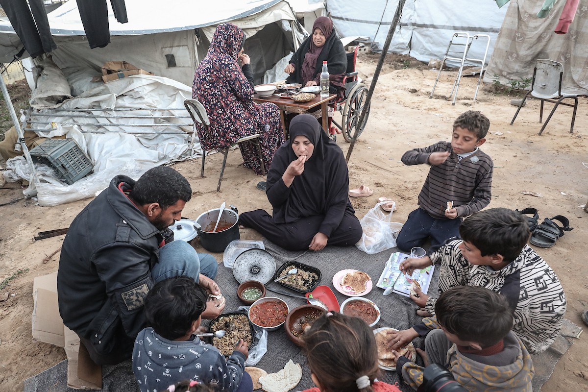 عائلة فلسطينية نازحة تتناول فطورها خلال شهر رمضان داخل خيمة متداعية في مخيم النصيرات للاجئين وسط قطاع غزة. تواجه العائلات النازحة ظروفًا معيشية قاسية نتيجة الحرب، مع انعدام الدخل ونقص حاد في المساعدات الإنسانية، 26 فبراير/شباط 2026. تصوير: معز صالحي