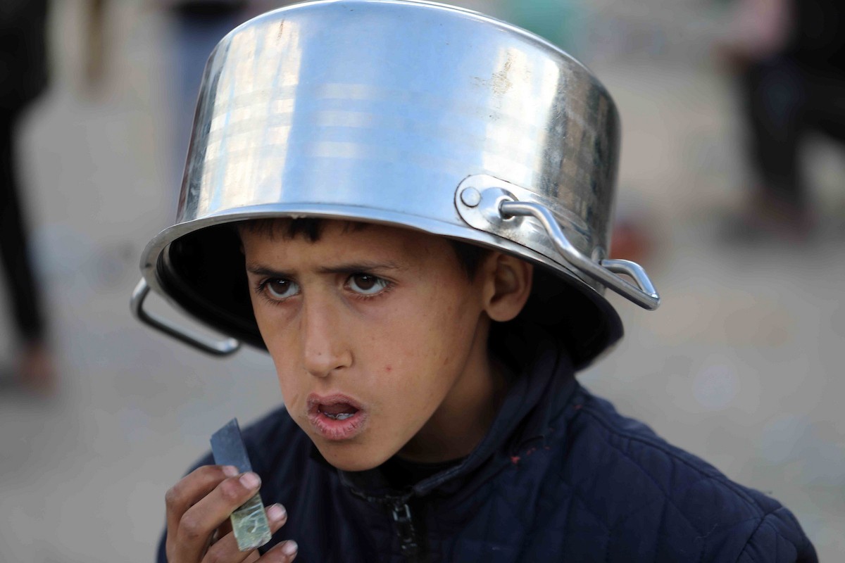 تجمع فلسطينيون نازحون، بينهم أطفال ونساء، حاملين أوعية طعام لتلقي وجبات ساخنة وزعتها جمعيات خيرية قبل الإفطار في مدينة غزة في 27 فبراير/شباط 2026.صورة: عمر أشتوي