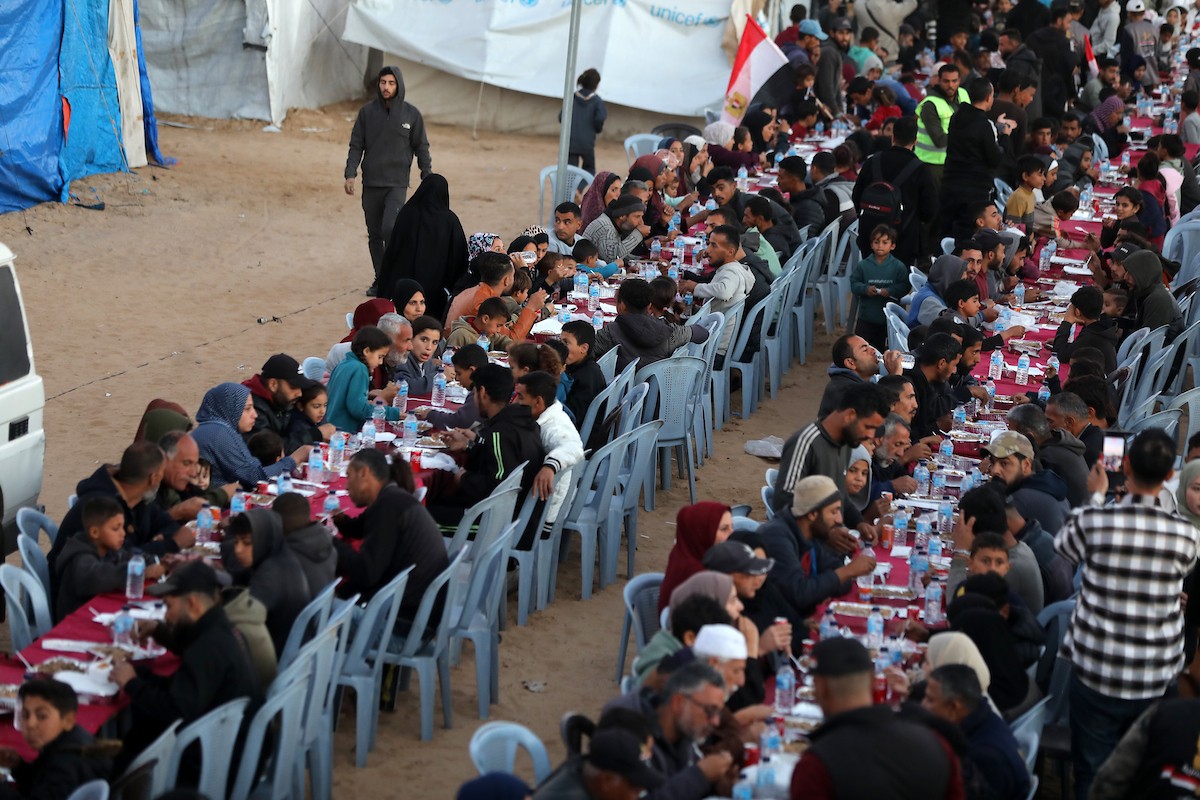يتجمع فلسطينيون نازحون لتناول وجبة الإفطار، وهي وجبة كسر الصيام، خلال شهر رمضان المبارك في مخيم خيام يؤويهم، بحي الزهراء وسط قطاع غزة، يوم السبت 21 فبراير/شباط 2026. تصوير: عمر أشتوي