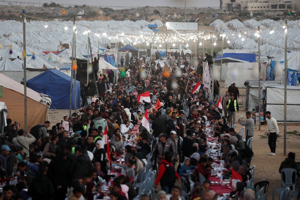 يتجمع فلسطينيون نازحون لتناول وجبة الإفطار، وهي وجبة كسر الصيام، خلال شهر رمضان المبارك في مخيم خيام يؤويهم، بحي الزهراء وسط قطاع غزة، يوم السبت 21 فبراير/شباط 2026. تصوير: عمر أشتوي