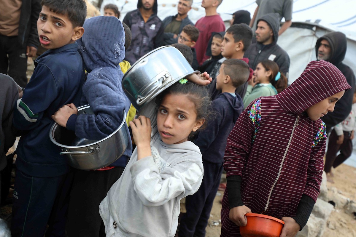 تجمع فلسطينيون نازحون، بينهم أطفال ونساء، حاملين أوعية طعام لتلقي وجبات ساخنة وزعتها جمعيات خيرية قبل الإفطار في مدينة غزة في 27 فبراير/شباط 2026.صورة: عمر أشتوي