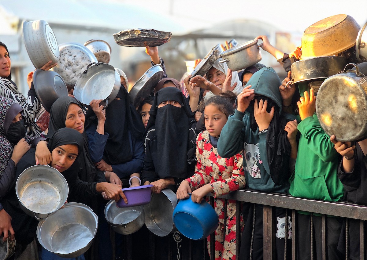 فلسطينيون نازحون يكافحون للحصول على طعام مُتبرع به للإفطار، وجبة كسر الصيام، في اليوم الرابع من شهر رمضان المبارك في مطبخ مجتمعي في خان يونس، قطاع غزة، 21 فبراير/شباط 2026. تصوير: طارق محمد/(APA Images)