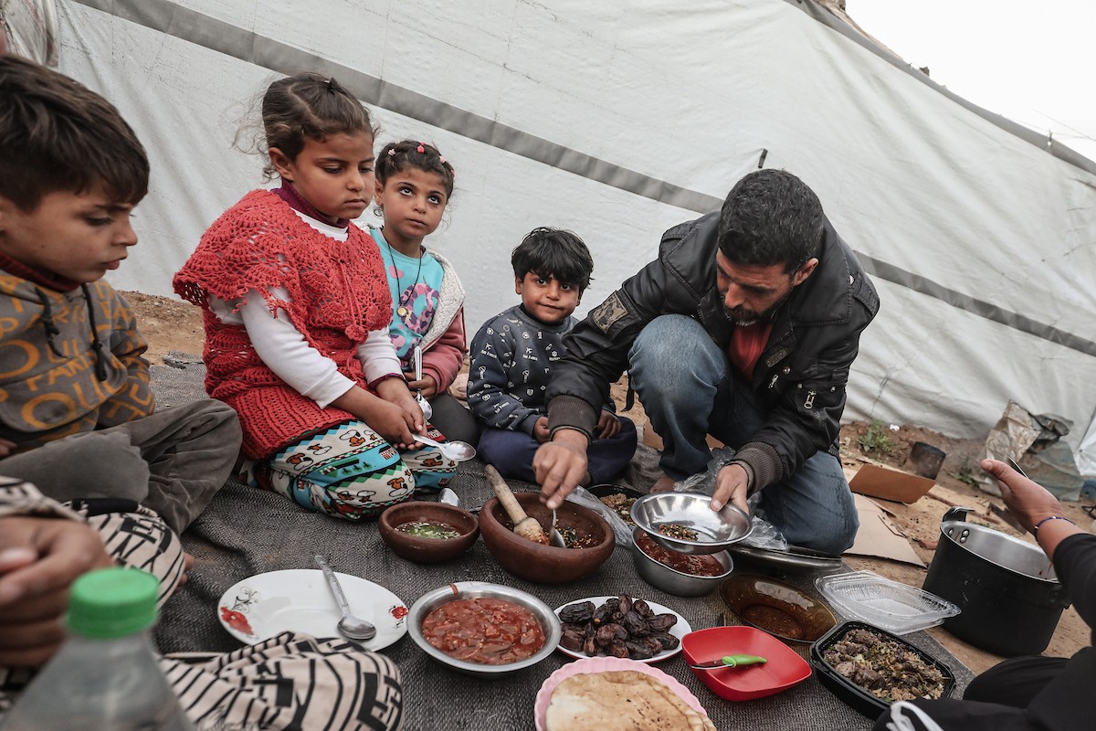 عائلة فلسطينية نازحة تتناول فطورها خلال شهر رمضان داخل خيمة متداعية في مخيم النصيرات للاجئين وسط قطاع غزة. تواجه العائلات النازحة ظروفًا معيشية قاسية نتيجة الحرب، مع انعدام الدخل ونقص حاد في المساعدات الإنسانية، 26 فبراير/شباط 2026. تصوير: معز صالحي