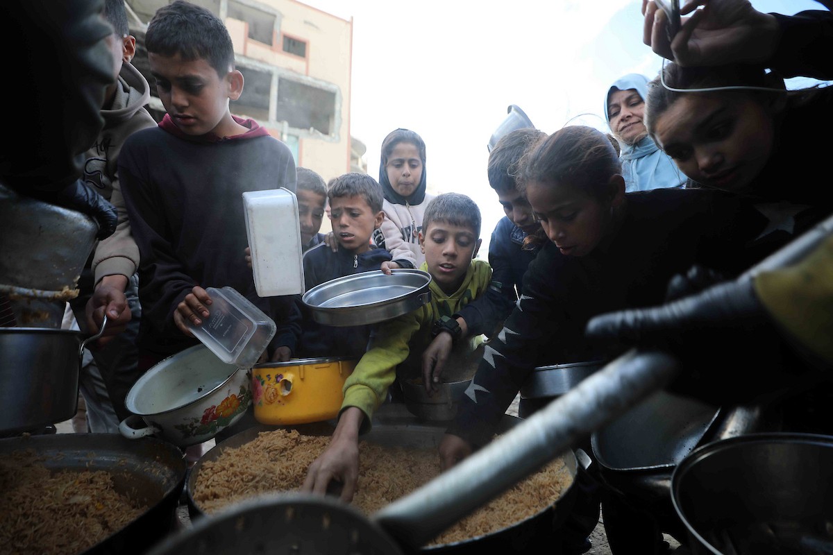تجمع فلسطينيون نازحون، بينهم أطفال ونساء، حاملين أوعية طعام لتلقي وجبات ساخنة وزعتها جمعيات خيرية قبل الإفطار في مدينة غزة في 27 فبراير/شباط 2026.صورة: عمر أشتوي