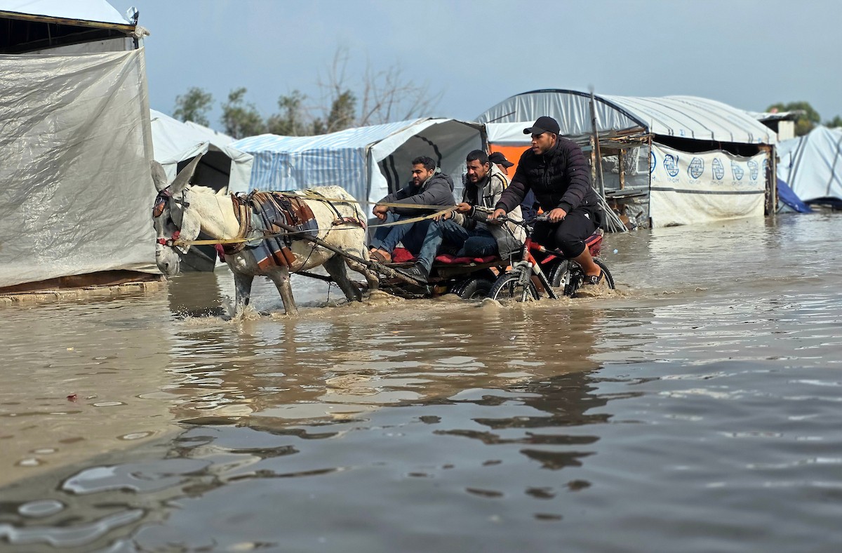 يحاول الفلسطينيون التنقل بعد أن غمرت مياه الأمطار الشوارع وخيام النازحين في خان يونس، جنوب قطاع غزة، في 24 فبراير/شباط 2026. وقد دُمرت البنية التحتية في قطاع غزة على نطاق واسع جراء الحرب والهجمات الإسرائيلية. (صورة: طارق محمد)
