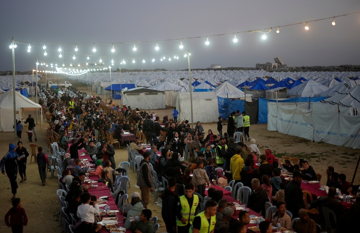 يتجمع فلسطينيون نازحون لتناول وجبة الإفطار، وهي وجبة كسر الصيام، خلال شهر رمضان المبارك في مخيم خيام يؤويهم، بحي الزهراء وسط قطاع غزة، يوم السبت 21 فبراير/شباط 2026. تصوير: عمر أشتوي