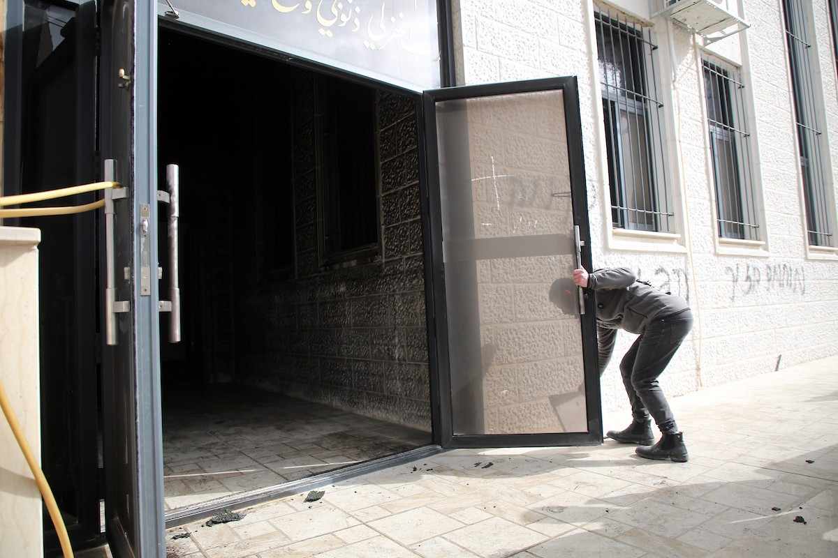 يتفقد فلسطينيون المدخل المحترق لمسجد أبو بكر الصديق في قرية تل، غرب نابلس بالضفة الغربية، في 23 فبراير/شباط 2026، عقب هجوم نُسب إلى مستوطنين يهود. صورة: محمد ناصر