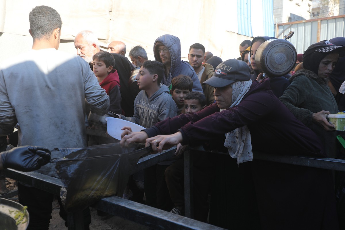 يتجمع فلسطينيون لتناول وجبة ساخنة وزعتها إحدى الجمعيات الخيرية، وسط أزمة غذائية مستمرة بسبب محدودية المساعدات الإنسانية خلال شهر رمضان في مخيم النصيرات للاجئين وسط قطاع غزة. ٢٣ فبرايرشباط ٢٠٢٦. تصوير معز صالحي