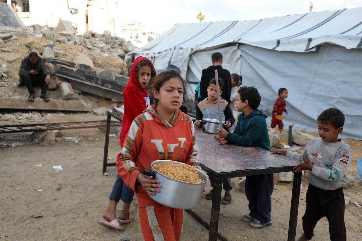 تجمع فلسطينيون نازحون، بينهم أطفال ونساء، حاملين أوعية طعام لتلقي وجبات ساخنة وزعتها جمعيات خيرية قبل الإفطار في مدينة غزة في 27 فبراير/شباط 2026.صورة: عمر أشتوي