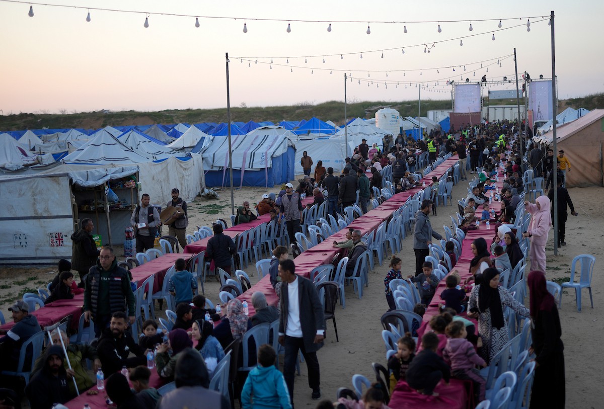 يتجمع فلسطينيون نازحون لتناول وجبة الإفطار، وهي وجبة كسر الصيام، خلال شهر رمضان المبارك في مخيم خيام يؤويهم، بحي الزهراء وسط قطاع غزة، يوم السبت 21 فبراير/شباط 2026. تصوير: عمر أشتوي