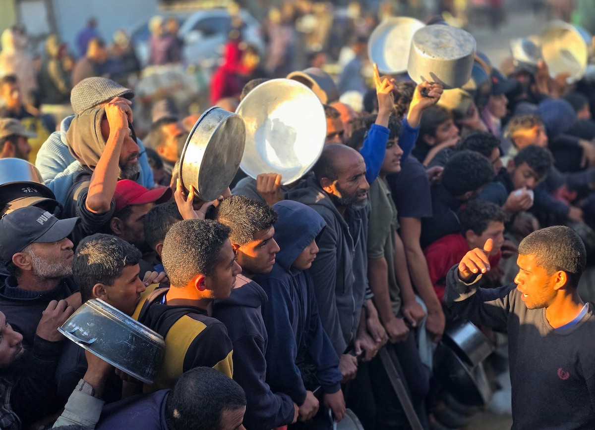 فلسطينيون نازحون يكافحون للحصول على طعام مُتبرع به للإفطار، وجبة كسر الصيام، في اليوم الرابع من شهر رمضان المبارك في مطبخ مجتمعي في خان يونس، قطاع غزة، 21 فبراير/شباط 2026. تصوير: طارق محمد/(APA Images)
