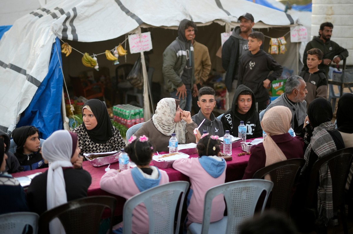 يتجمع فلسطينيون نازحون لتناول وجبة الإفطار، وهي وجبة كسر الصيام، خلال شهر رمضان المبارك في مخيم خيام يؤويهم، بحي الزهراء وسط قطاع غزة، يوم السبت 21 فبراير/شباط 2026. تصوير: عمر أشتوي