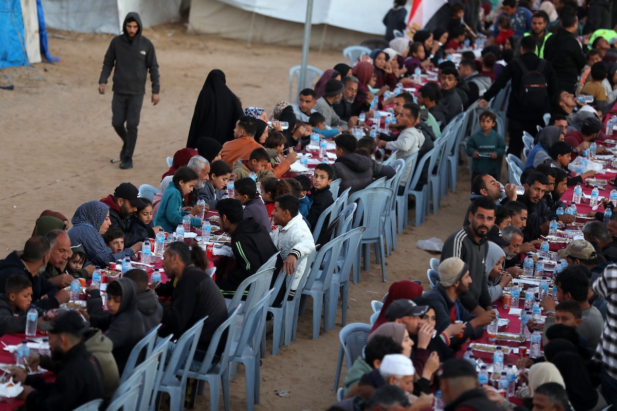 يتجمع فلسطينيون نازحون لتناول وجبة الإفطار، وهي وجبة كسر الصيام، خلال شهر رمضان المبارك في مخيم خيام يؤويهم، بحي الزهراء وسط قطاع غزة، يوم السبت 21 فبراير/شباط 2026. تصوير: عمر أشتوي
