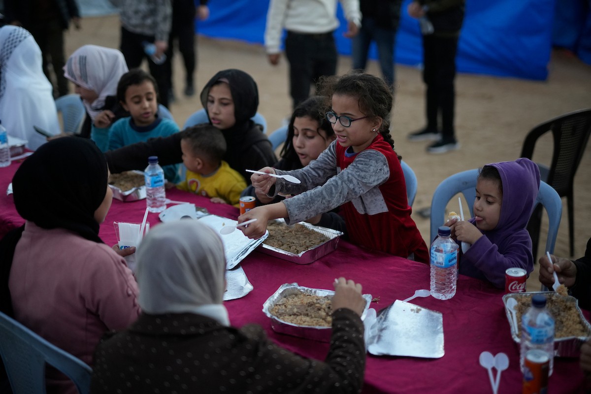 يتجمع فلسطينيون نازحون لتناول وجبة الإفطار، وهي وجبة كسر الصيام، خلال شهر رمضان المبارك في مخيم خيام يؤويهم، بحي الزهراء وسط قطاع غزة، يوم السبت 21 فبراير/شباط 2026. تصوير: عمر أشتوي