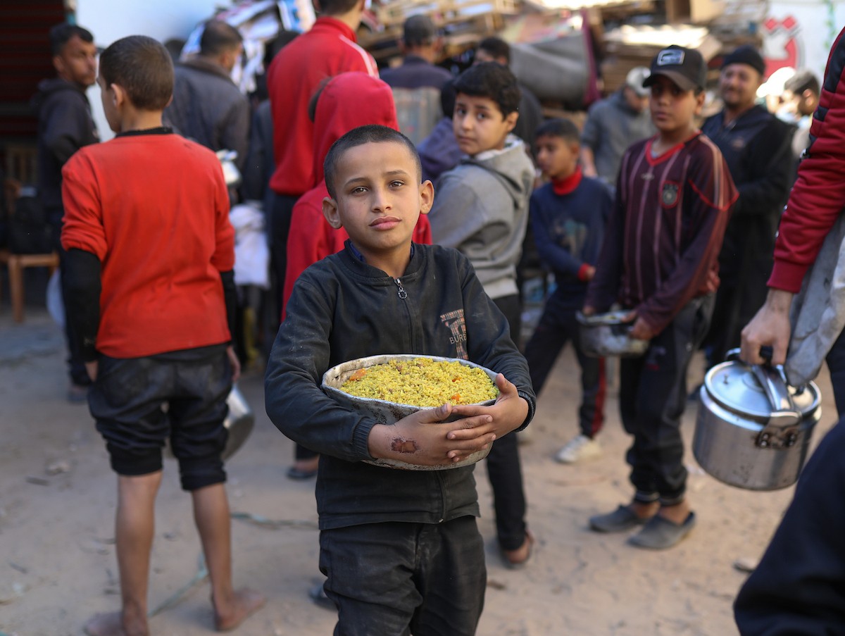 يتجمع فلسطينيون نازحون لتناول وجبة إفطارهم الرمضانية في مطبخ خيري بمخيم النصيرات للاجئين وسط قطاع غزة، في 24 فبراير/شباط 2026. ويواجه النازحون ظروفًا معيشية قاسية نتيجة انعدام الدخل ونقص المساعدات الإنسانية. (صورة: رمزي أبو عامر / apaimages)