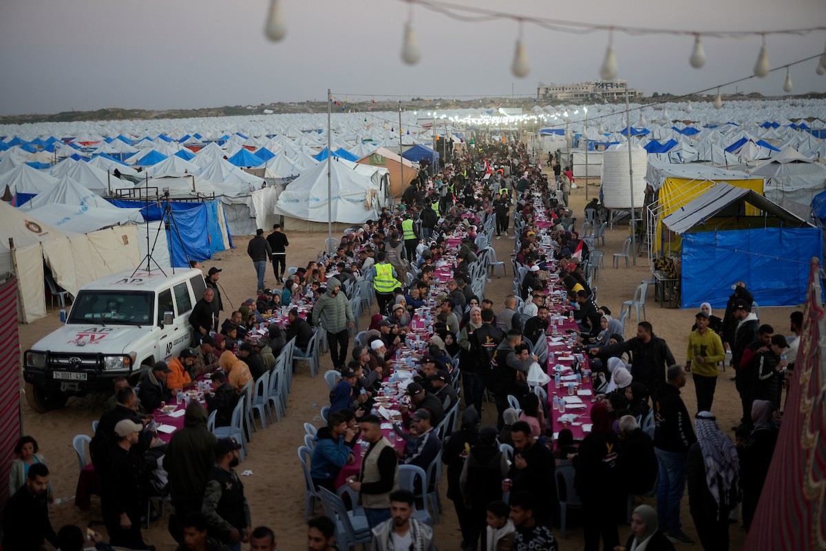 يتجمع فلسطينيون نازحون لتناول وجبة الإفطار، وهي وجبة كسر الصيام، خلال شهر رمضان المبارك في مخيم خيام يؤويهم، بحي الزهراء وسط قطاع غزة، يوم السبت 21 فبراير/شباط 2026. تصوير: عمر أشتوي